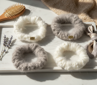 Four fluffy scrunchies on a marble surface with a hairbrush and lavender sprigs.
