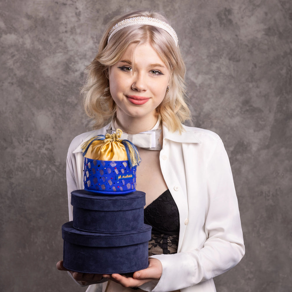 Blonde-haired smiling girl is holding Malkiele designer blue round boxes.