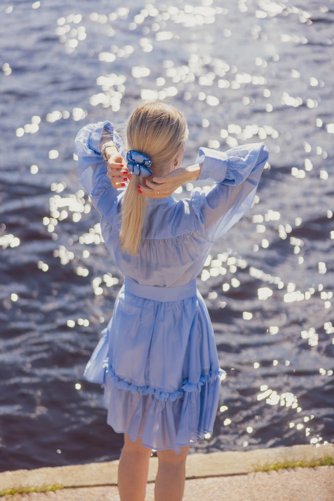 Blond girl in blue dress is making stylish ponytail in 3 sec with light blue  silk scrunchie by malkiele sustainable designer