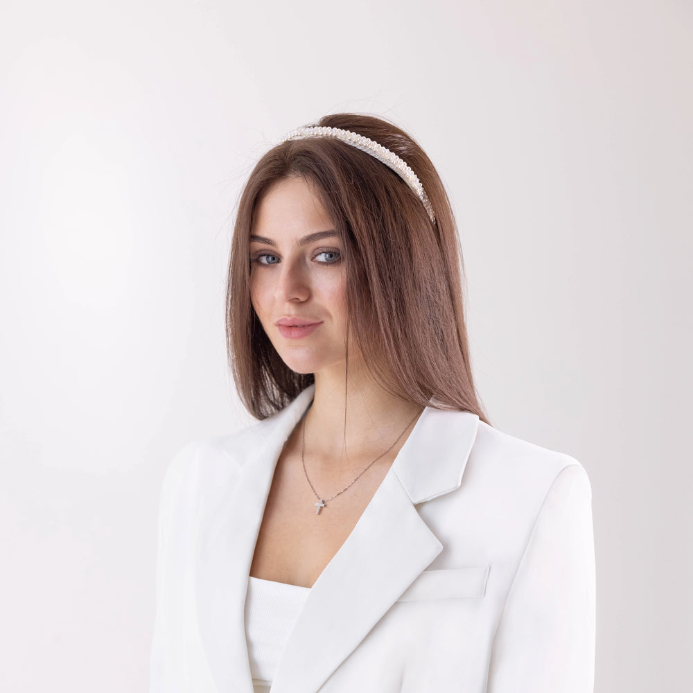 Dark-haired smiling girl in white jacket is wearing Malkiele designer white silk knit headbands, embellished with pearls from Swarovski, name Victorious.