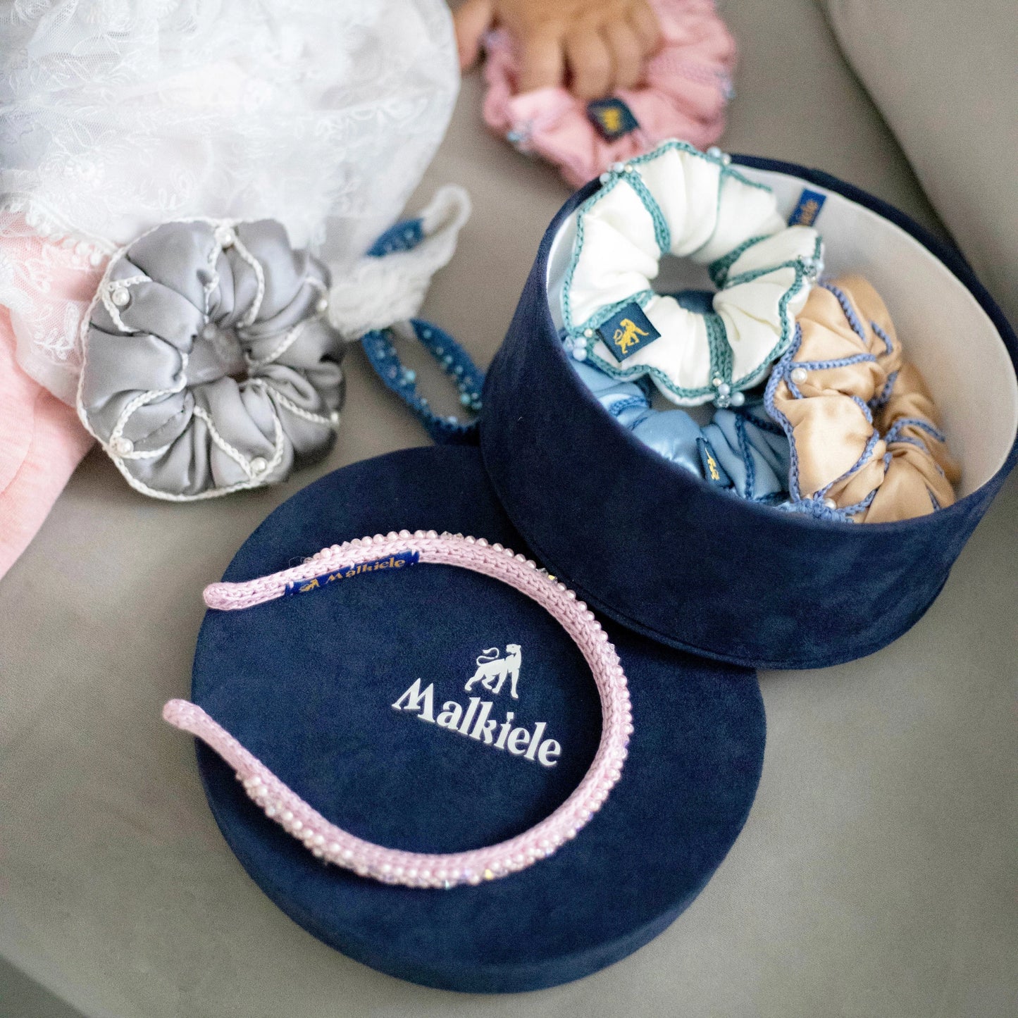 Malkiele designer, gift set consists of dark blue round velvet box with open cover, light blue silk hair tie, blue silk scrunchie and light pink silk knit headband, embellished with crystals from Swarovski®.