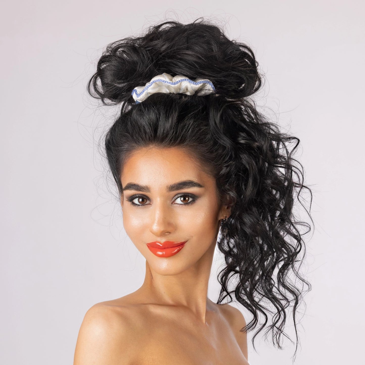 A black-haired smiling woman is wearing Malkiele designer white silk scrunchie, name Morning Passion.