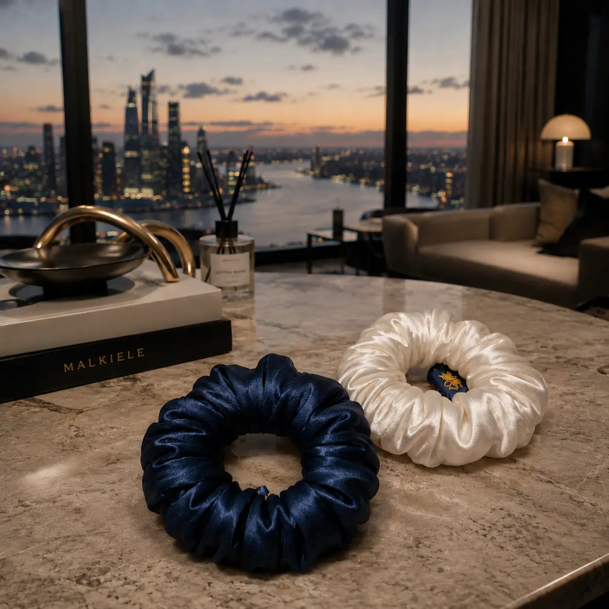 
                  
                    Two scrunchies, one blue and one white, on a table with a cityscape view in the background.
                  
                
