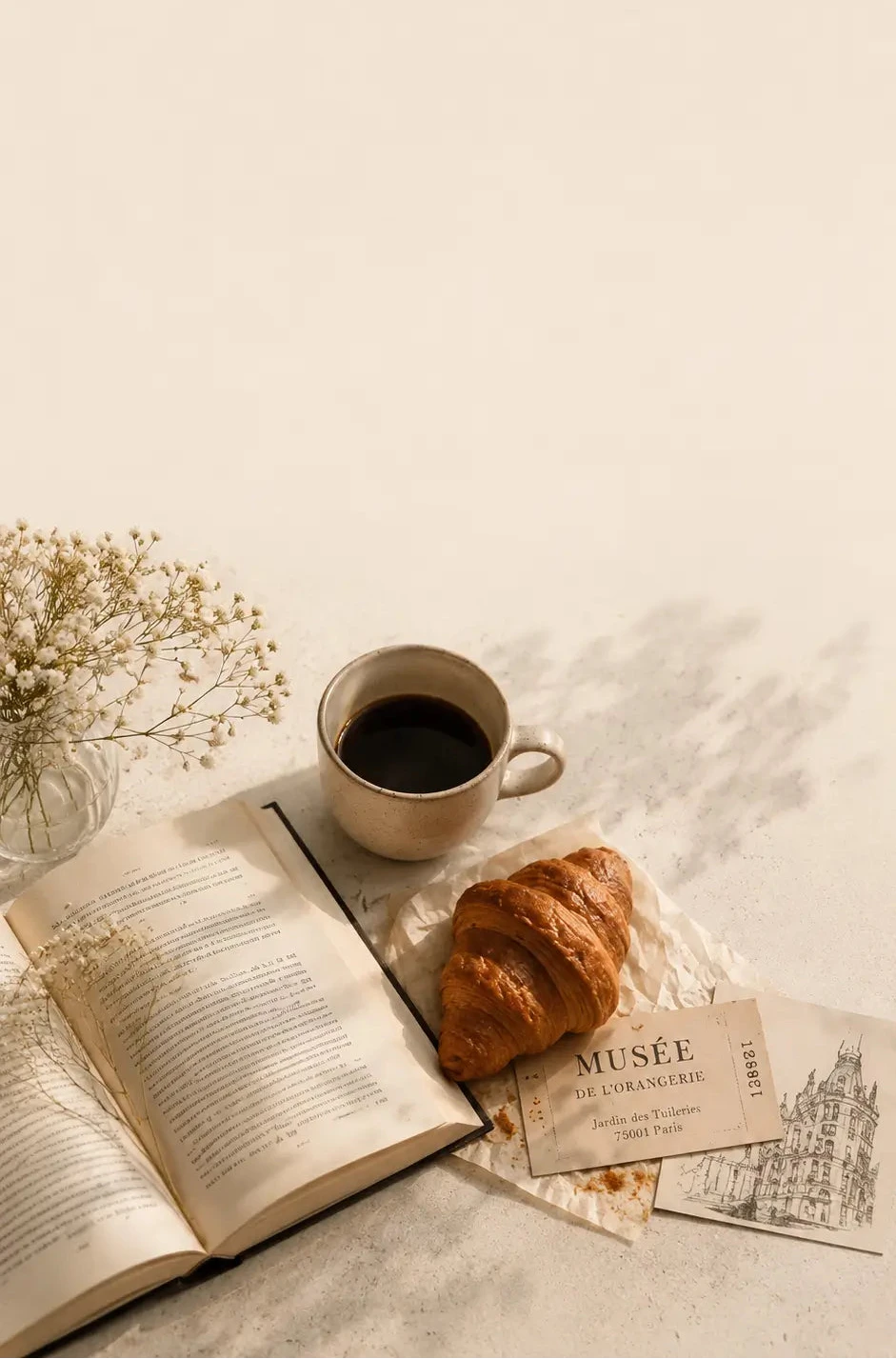 Open book, cup of coffee, croissant, and small bouquet on a light surface