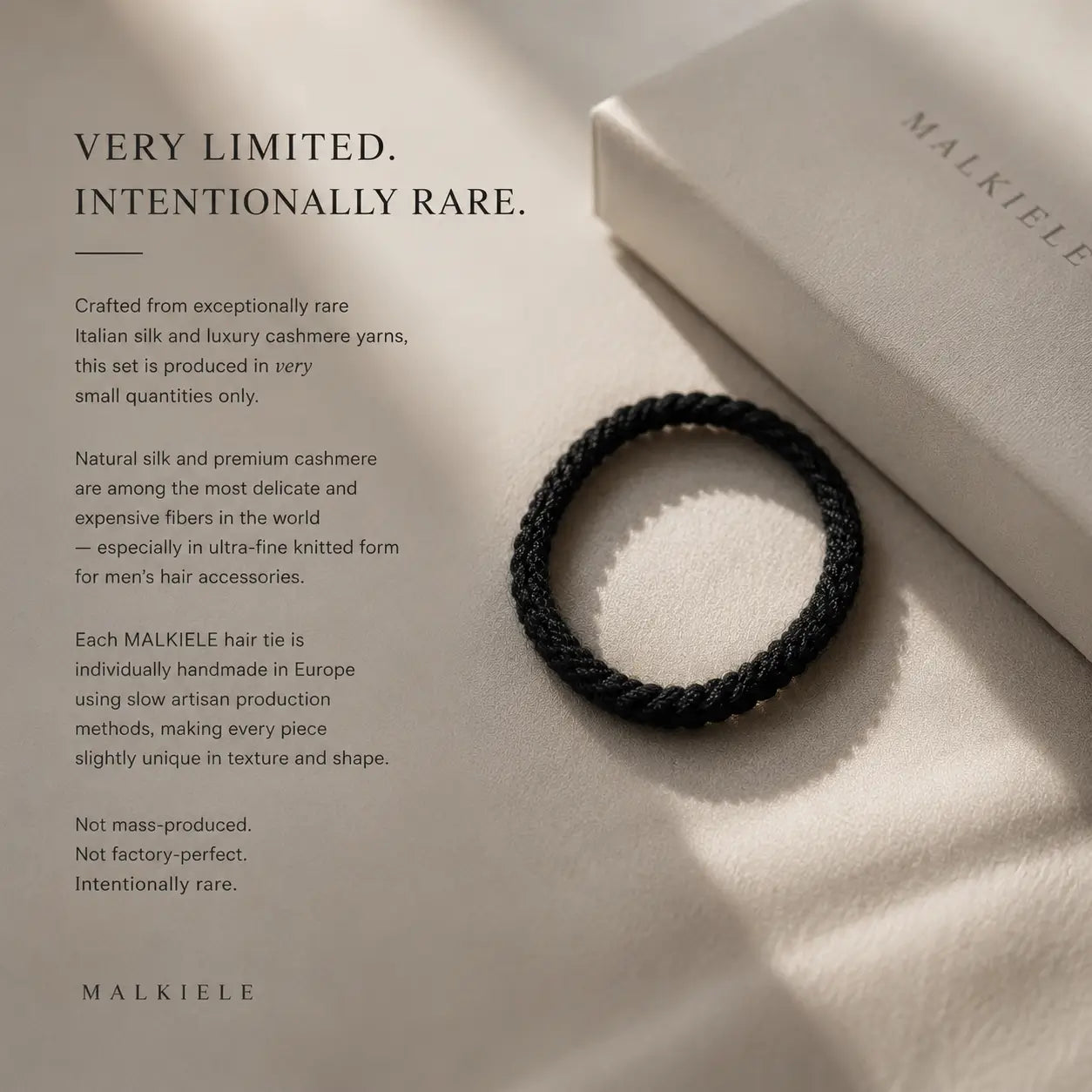 
                  
                    Black hair tie on a beige surface with text about exclusivity and craftsmanship, featuring the brand 'Malkiele'.
                  
                