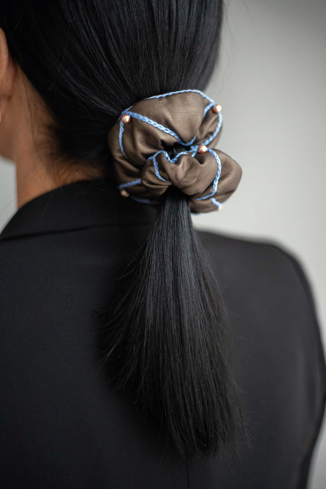 
                  
                    A black-haired woman, with stylish ponytail is wearing Malkiele designer brown vegan leather scrunchie, embellished with 6 pearls from Swarovski and light blue silk knit ribbon, back view, name Ambitious.
                  
                