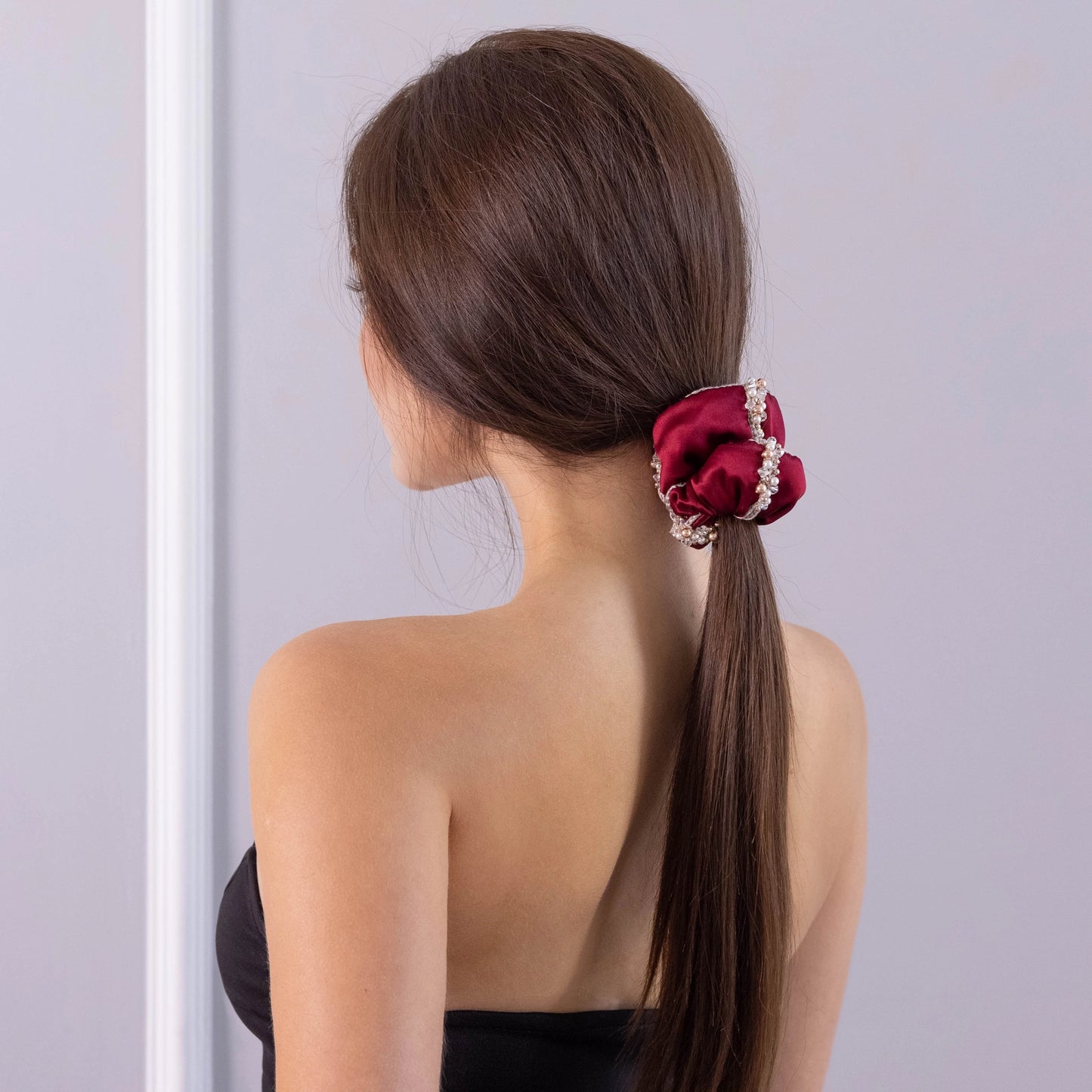 
                  
                    A dark-haired girl, view from the back, with stylish ponytail is wearing Malkiele designer burgundy silk scrunchie, embellished with crystals from Swarovski® and beige silk knit ribbon, name Elizabeth.
                  
                