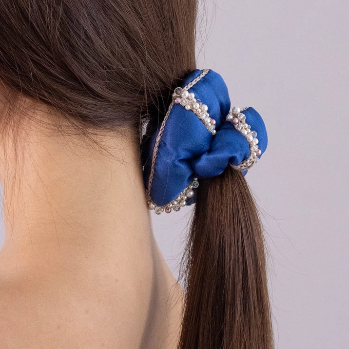 
                  
                    A dark-haired girl, view from the back, with stylish ponytail is wearing Malkiele designer blue silk scrunchie, embellished with crystals from Swarovski® and beige silk knit ribbon, name Elizabeth.
                  
                