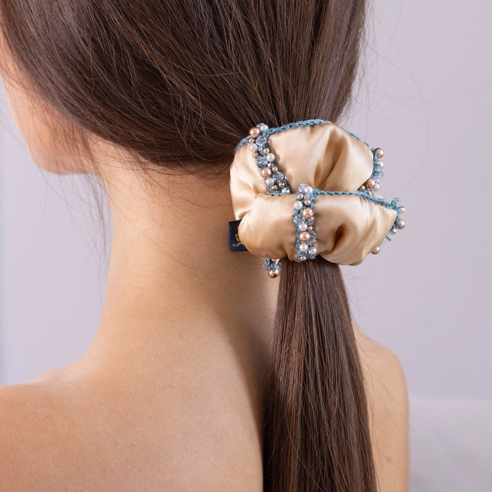 
                  
                    A dark-haired girl, view from the back, with stylish ponytail is wearing Malkiele designer beige silk scrunchie, embellished with crystals from Swarovski® and green silk knit ribbon, name Elizabeth.
                  
                