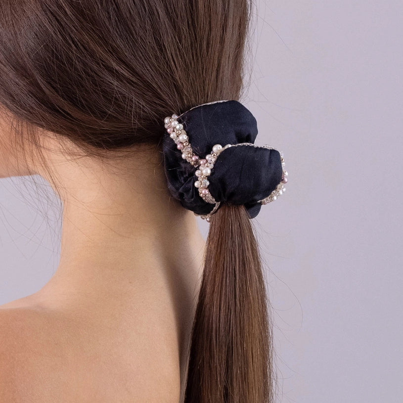 
                  
                    A dark-haired girl, view from the back, with stylish ponytail is wearing Malkiele designer black silk scrunchie, embellished with crystals from Swarovski® and beige silk knit ribbon, name Elizabeth.
                  
                