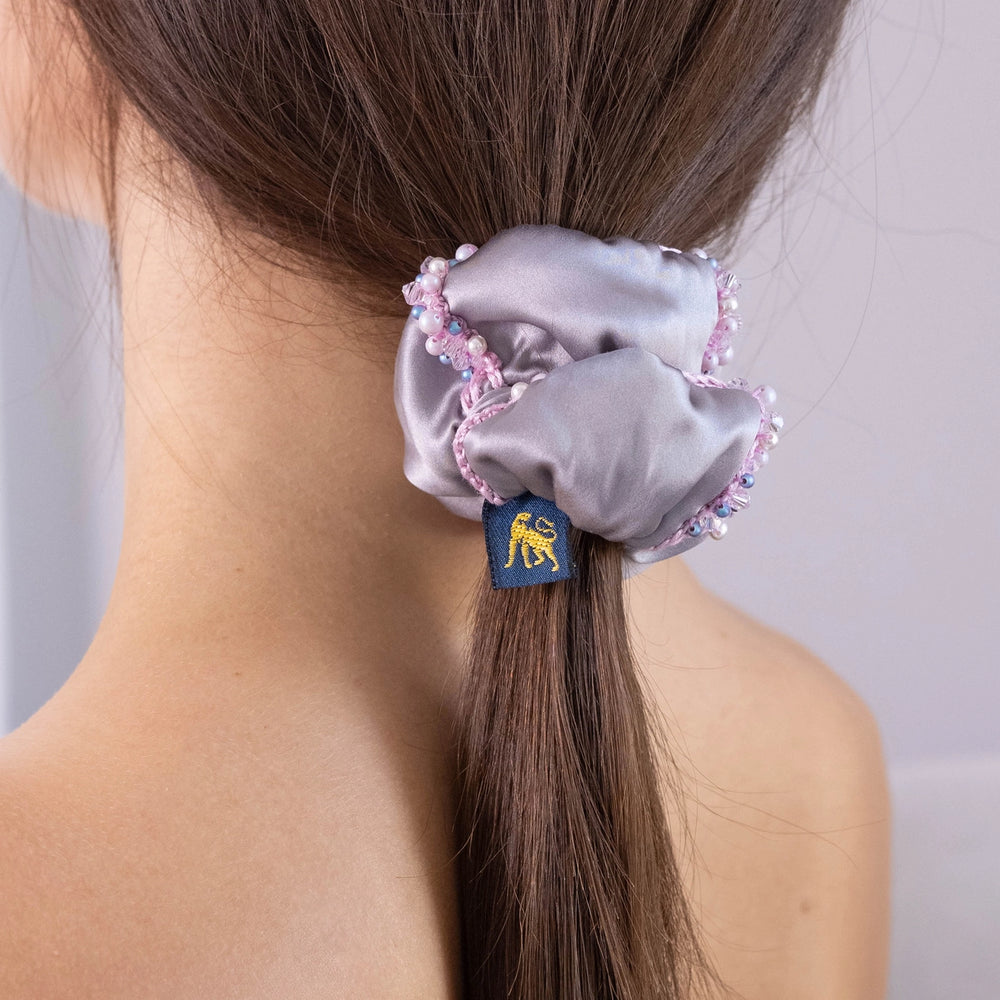 
                  
                    A dark-haired girl, view from the back, with stylish ponytail is wearing Malkiele designer grey silk scrunchie, embellished with crystals from Swarovski® and pink silk knit ribbon, name Elizabeth.
                  
                