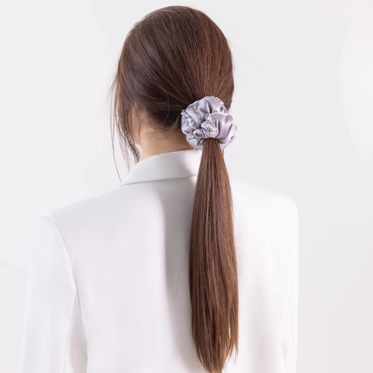 Dark-haired girl in white jacket, with stylish ponytail is wearing Malkiele designer grey silk scrunchie, embellished with crystals from Swarovski® and white silk knit ribbon, name Elizabeth.