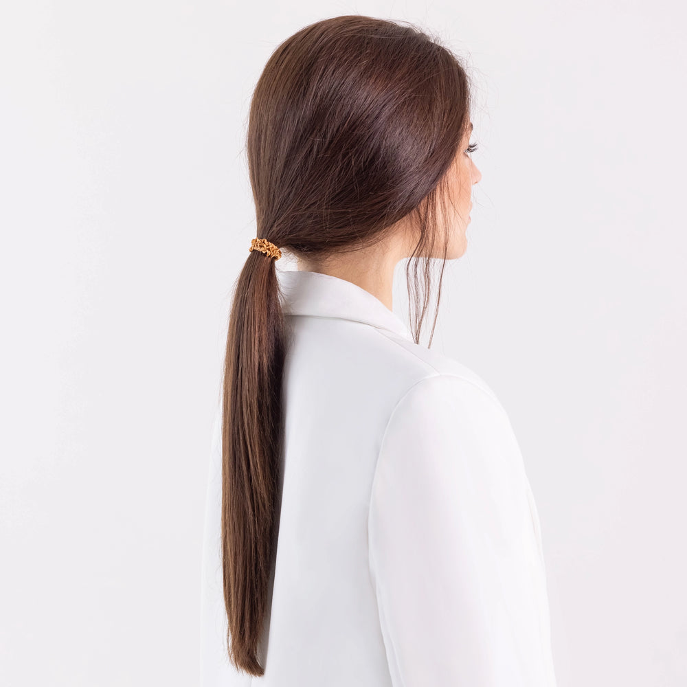 
                  
                    A dark-haired girl in white jacket, side view, with ponytail is wearing Malkiele designer beige silk gentle hair tie, name Finesse.
                  
                