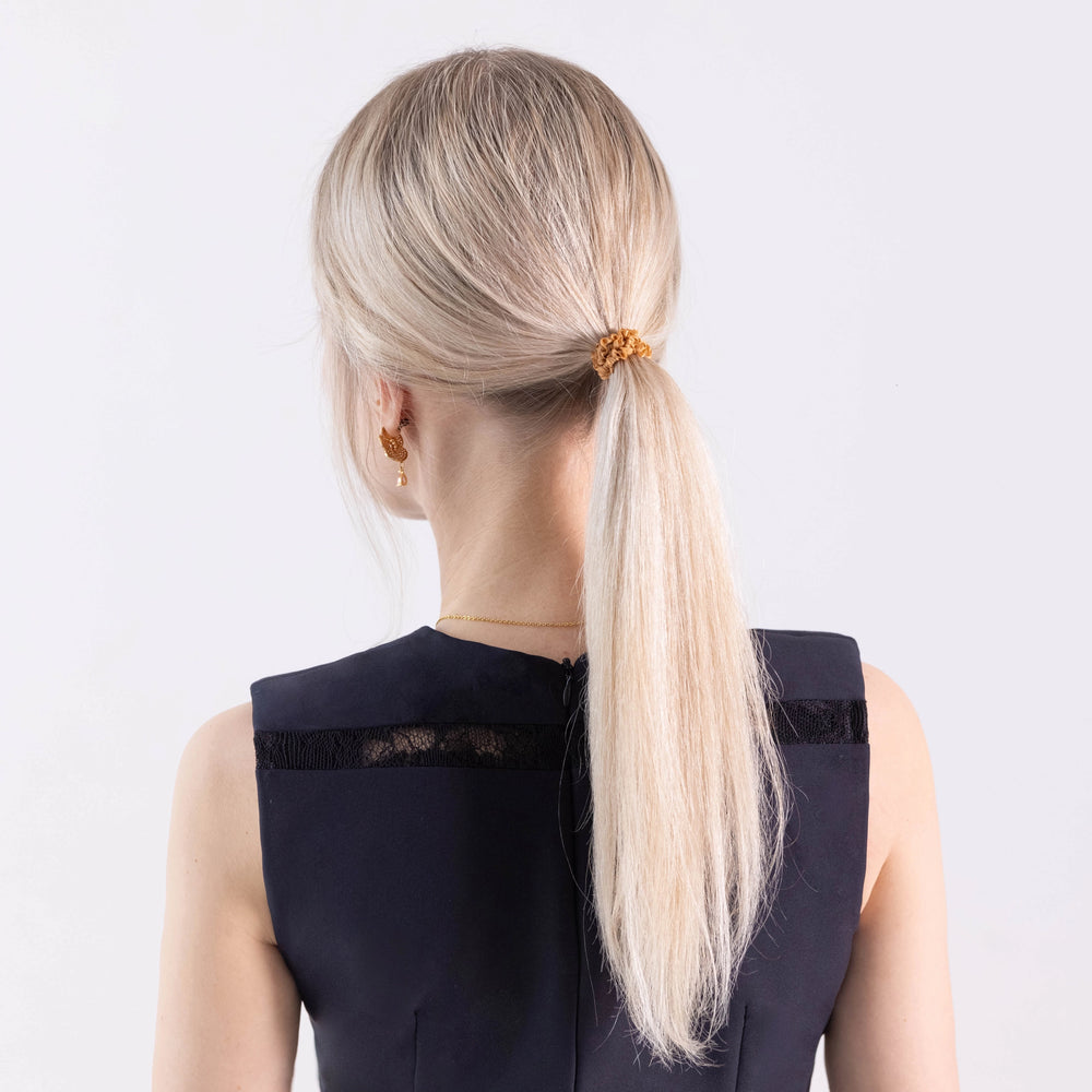 
                  
                    A blonde-haired girl in black dress, view from the back, with ponytail is wearing Malkiele designer beige silk gentle hair tie, name Finesse.
                  
                