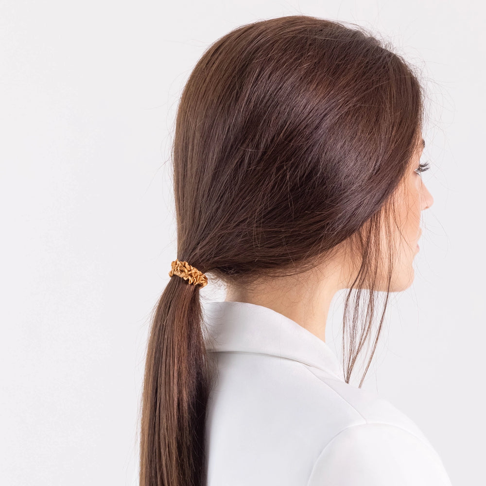 
                  
                    A dark-haired girl in white jacket, side view, details, with ponytail is wearing Malkiele designer beige silk gentle hair tie, name Finesse.
                  
                