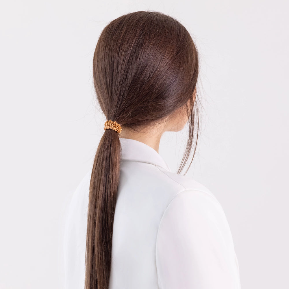 
                  
                    A dark-haired girl in white jacket, view from the back, with long ponytail is wearing Malkiele designer beige silk gentle hair tie, name Finesse.
                  
                