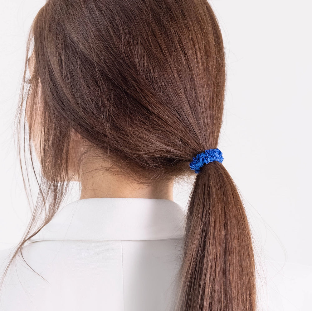 
                  
                    A dark-haired girl in white jacket, view from the back, details, with classic ponytail is wearing Malkiele designer royal blue silk gentle hair tie, name Finesse.
                  
                