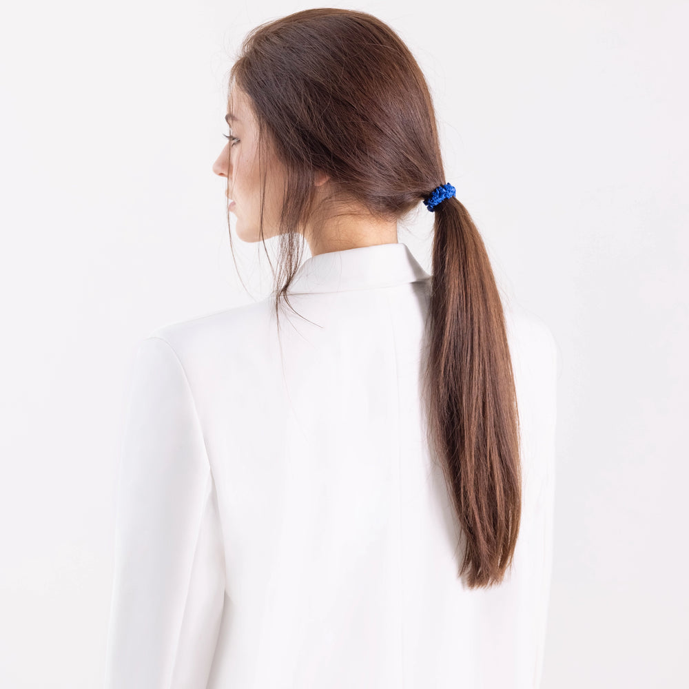 
                  
                    A dark-haired girl in white jacket, side view with half face, with classic ponytail is wearing Malkiele designer royal blue silk gentle hair tie, name Finesse.
                  
                