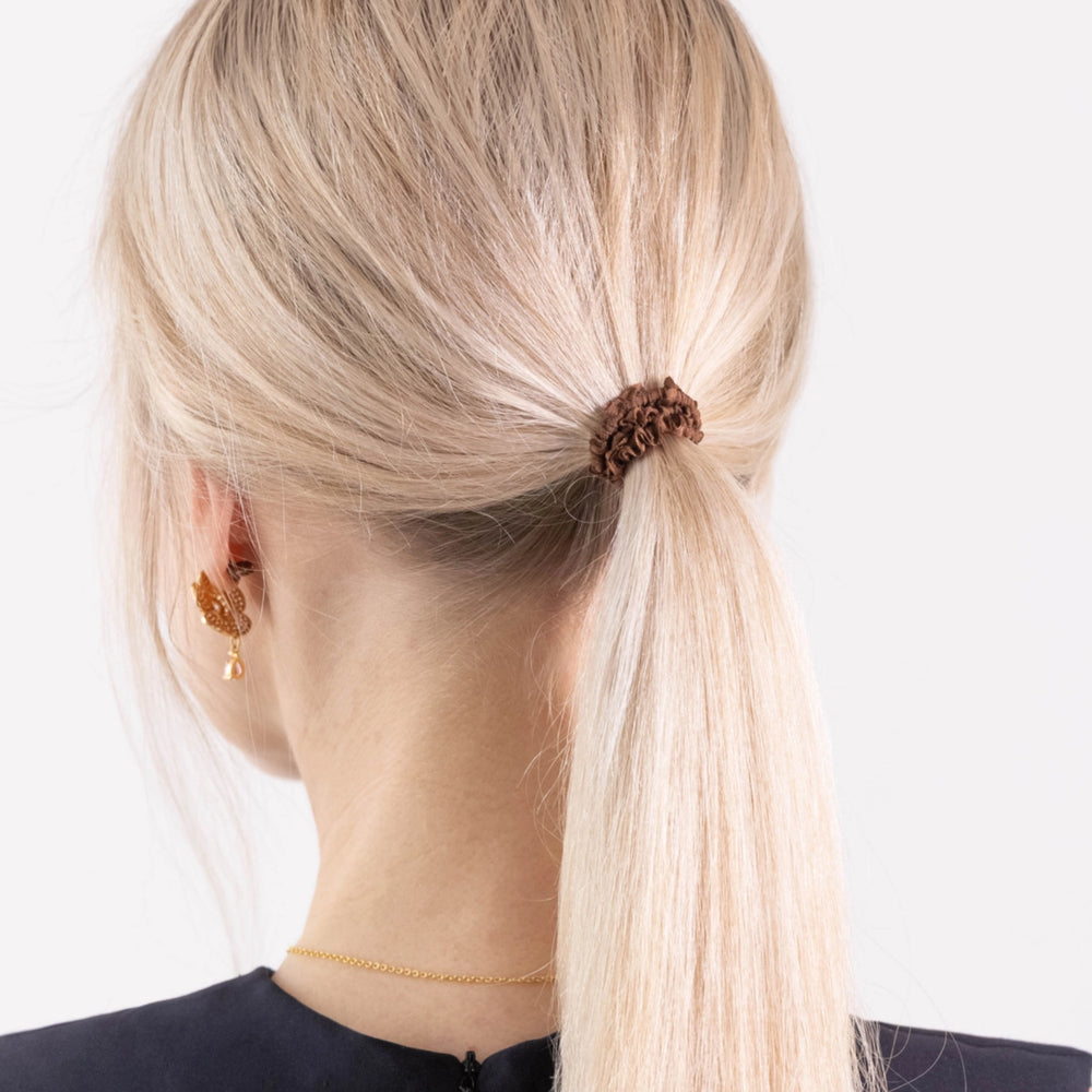 
                  
                    A blonde-haired girl in black dress, view from the back, details, with ponytail is wearing Malkiele designer brown silk gentle hair tie, name Finesse.
                  
                