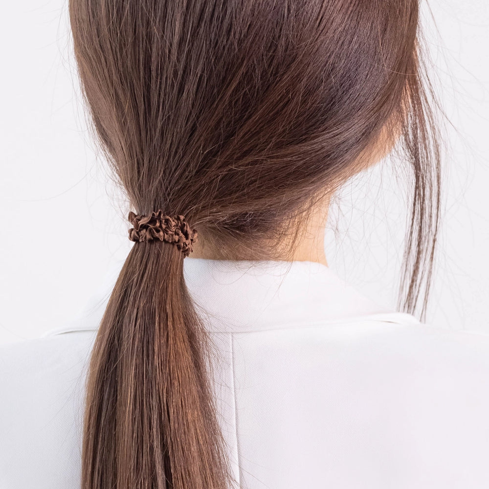 
                  
                    A dark-haired girl in white jacket, view from the back, details, with ponytail is wearing Malkiele designer brown silk gentle hair tie, name Finesse.
                  
                