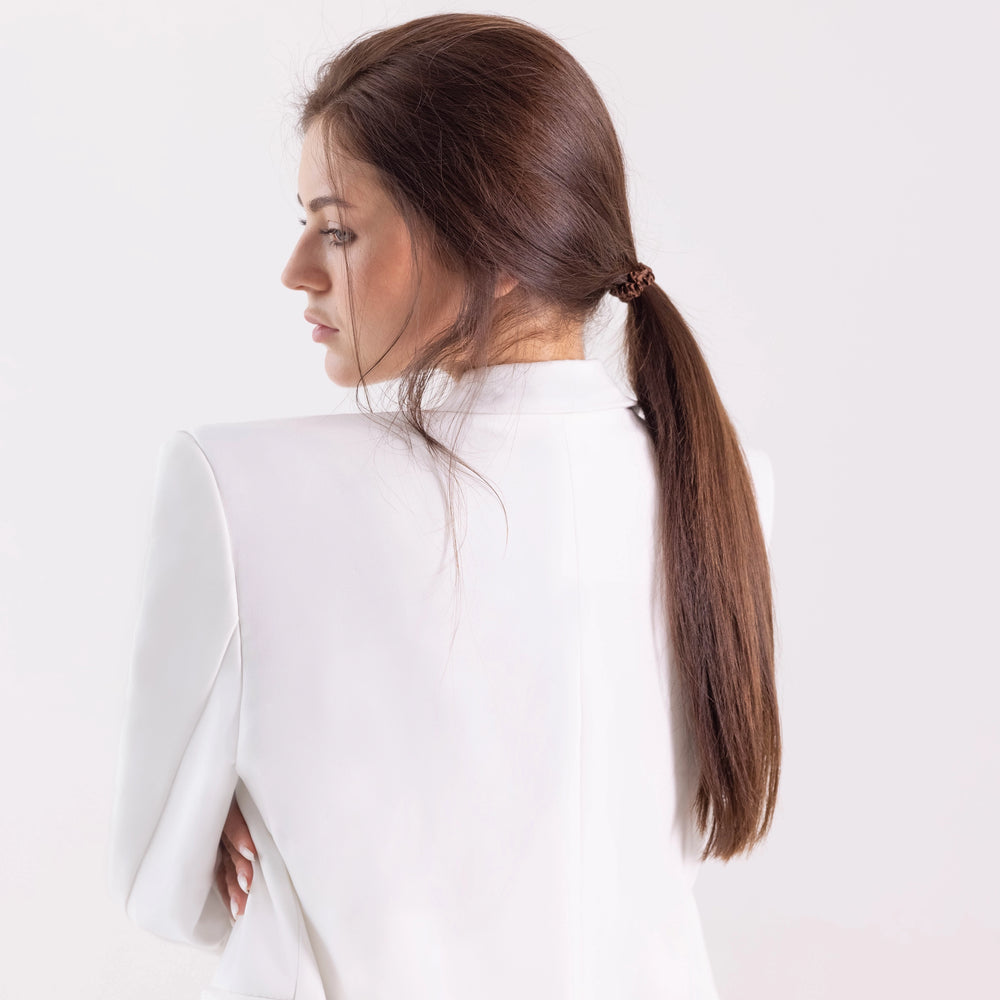 
                  
                    A dark-haired girl in white jacket, side view with half face, with ponytail is wearing Malkiele designer brown silk gentle hair tie, name Finesse.
                  
                