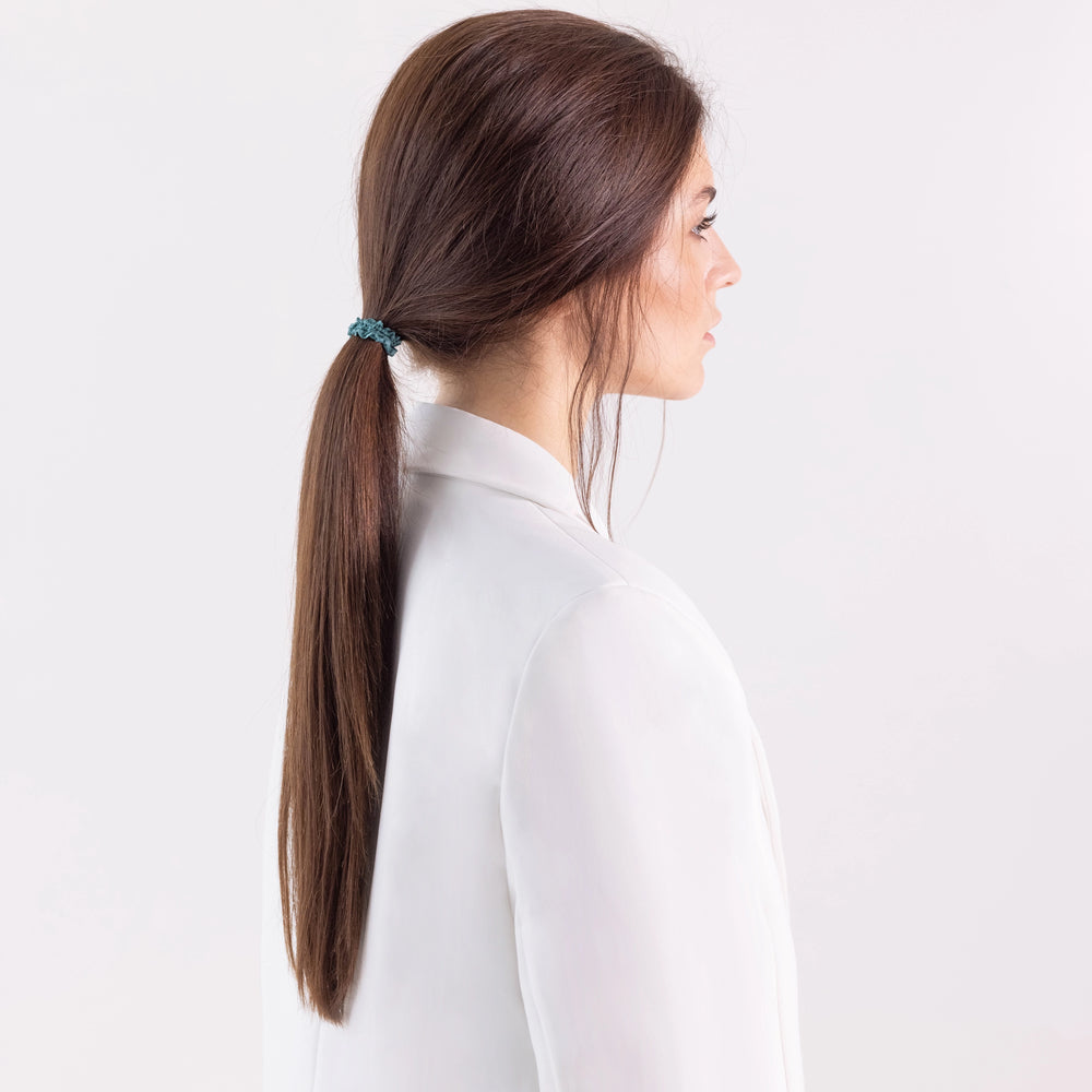 
                  
                    A dark-haired girl in white jacket, side view, with ponytail is wearing Malkiele designer green silk gentle hair tie, name Finesse.
                  
                