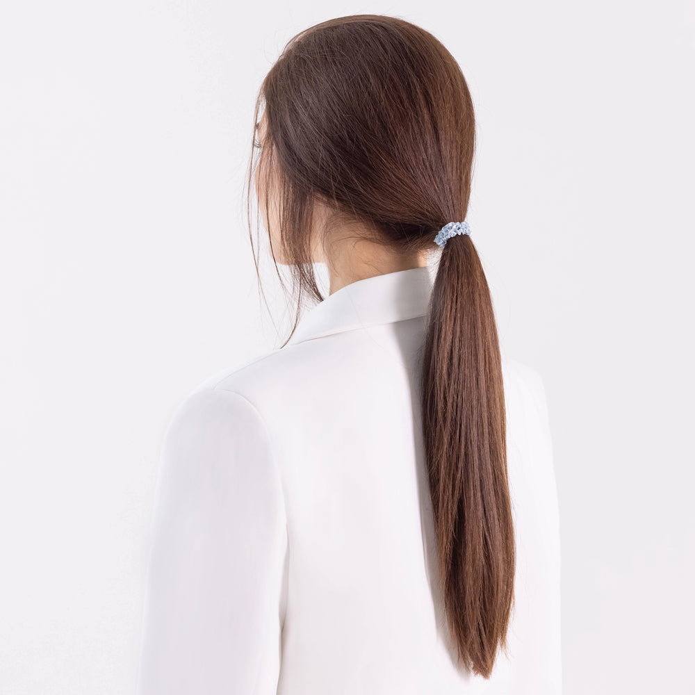 
                  
                    A dark-haired girl in white jacket, view from the back, with classic ponytail is wearing Malkiele designer grey silk gentle hair tie, name Finesse.
                  
                