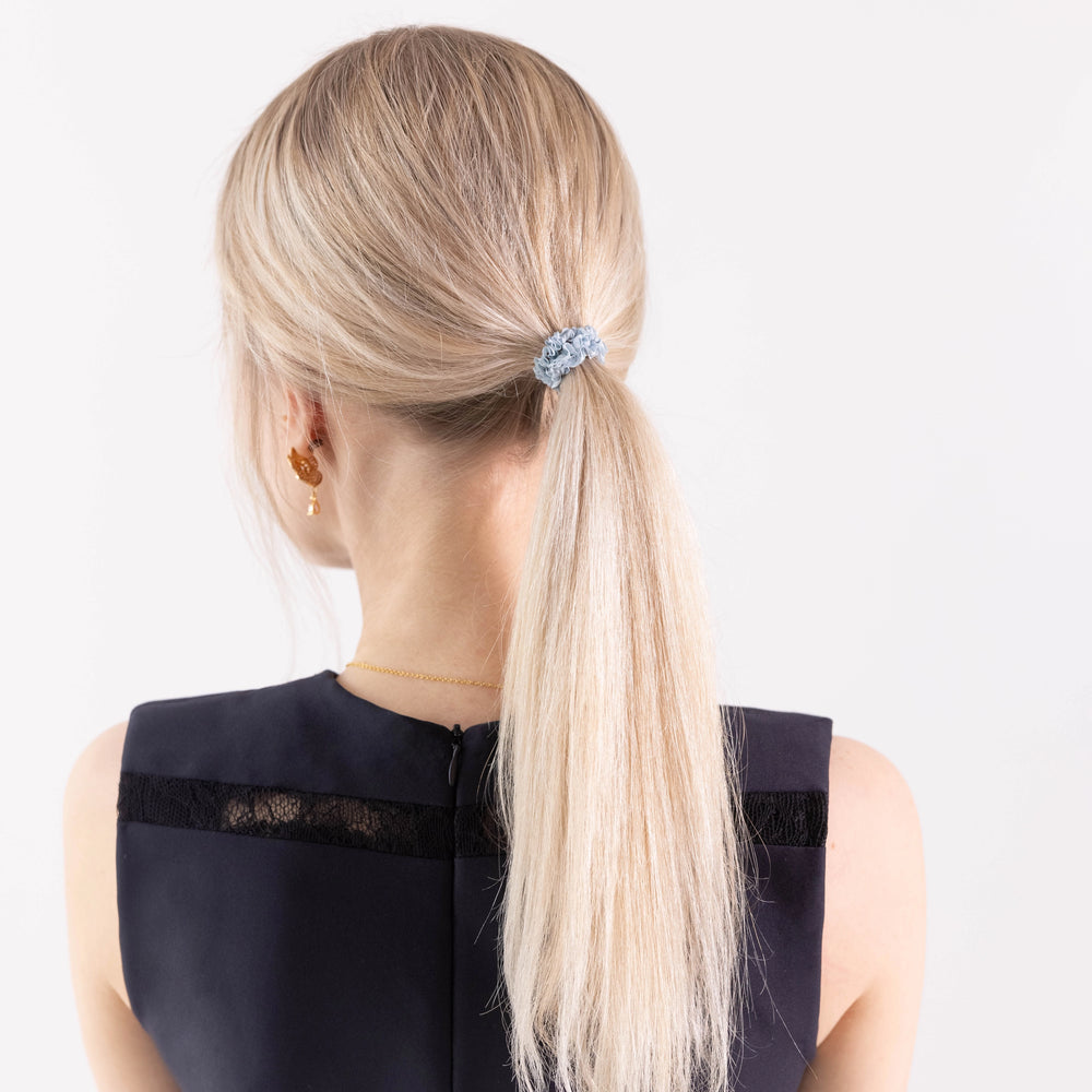 
                  
                    A blonde-haired girl in black dress, view from the back, with classic ponytail is wearing Malkiele designer grey silk gentle hair tie, name Finesse.
                  
                