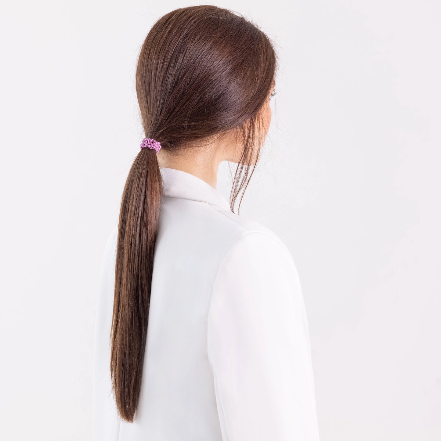 
                  
                    A dark-haired girl in white jacket, view from the back, with classic ponytail is wearing Malkiele designer pink silk gentle hair tie, name Finesse.
                  
                