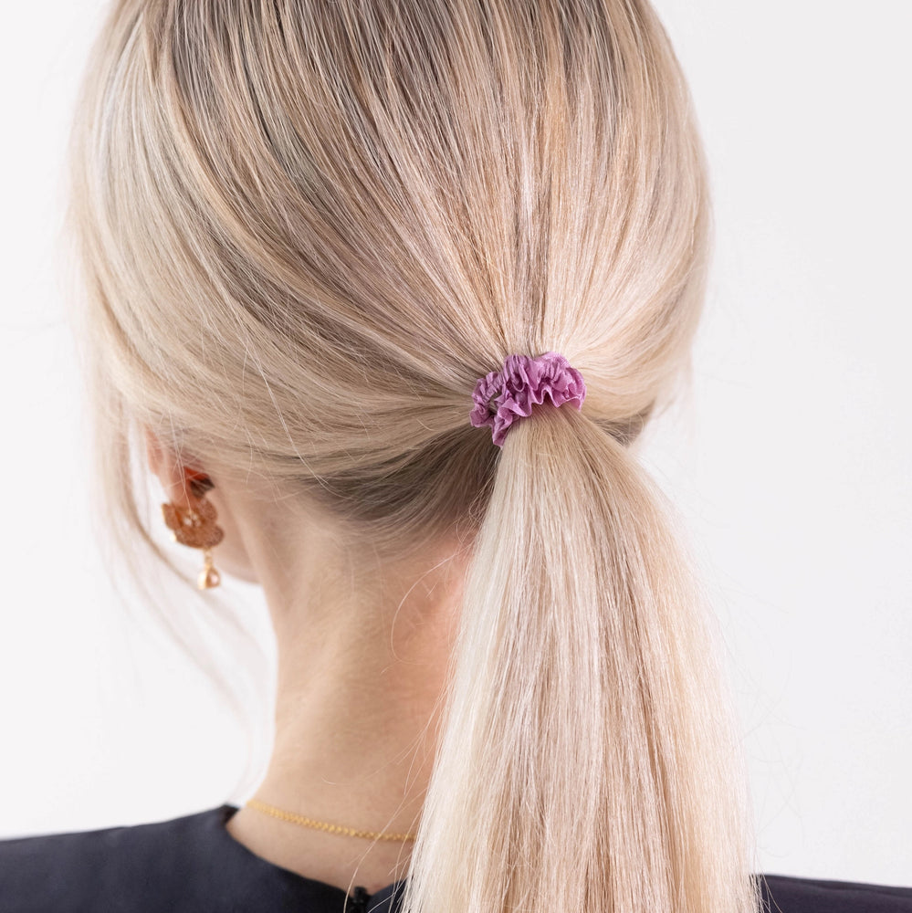 
                  
                    A blonde-haired girl in black dress, view from the back, details, with classic ponytail is wearing Malkiele designer pink silk gentle hair tie, name Finesse.
                  
                