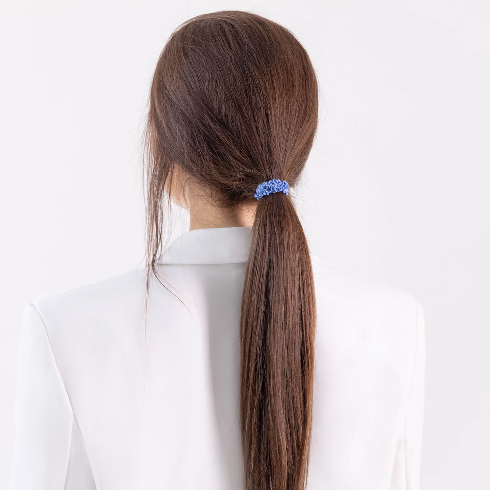 
                  
                    A dark-haired girl in white jacket, view from the back, with classic ponytail is wearing Malkiele designer light blue silk gentle hair tie, name Finesse.
                  
                