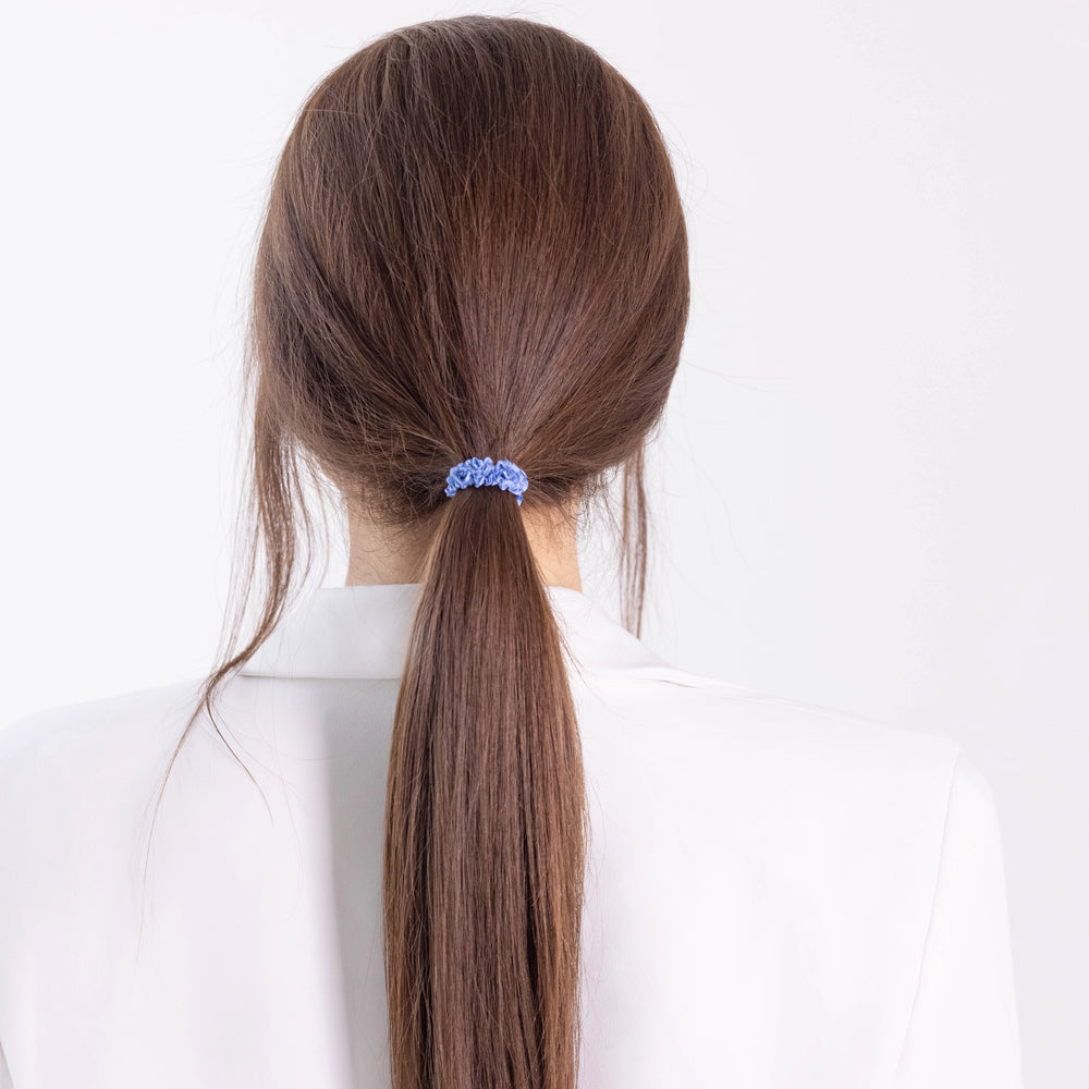 
                  
                    A dark-haired girl in white jacket, view from the back, with classic ponytail is wearing Malkiele designer light blue silk gentle hair tie, name Finesse.
                  
                