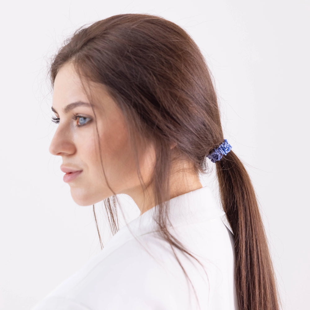 A dark-haired girl in white jacket, side view with half face, with classic ponytail is wearing Malkiele designer light blue silk gentle hair tie, name Finesse.