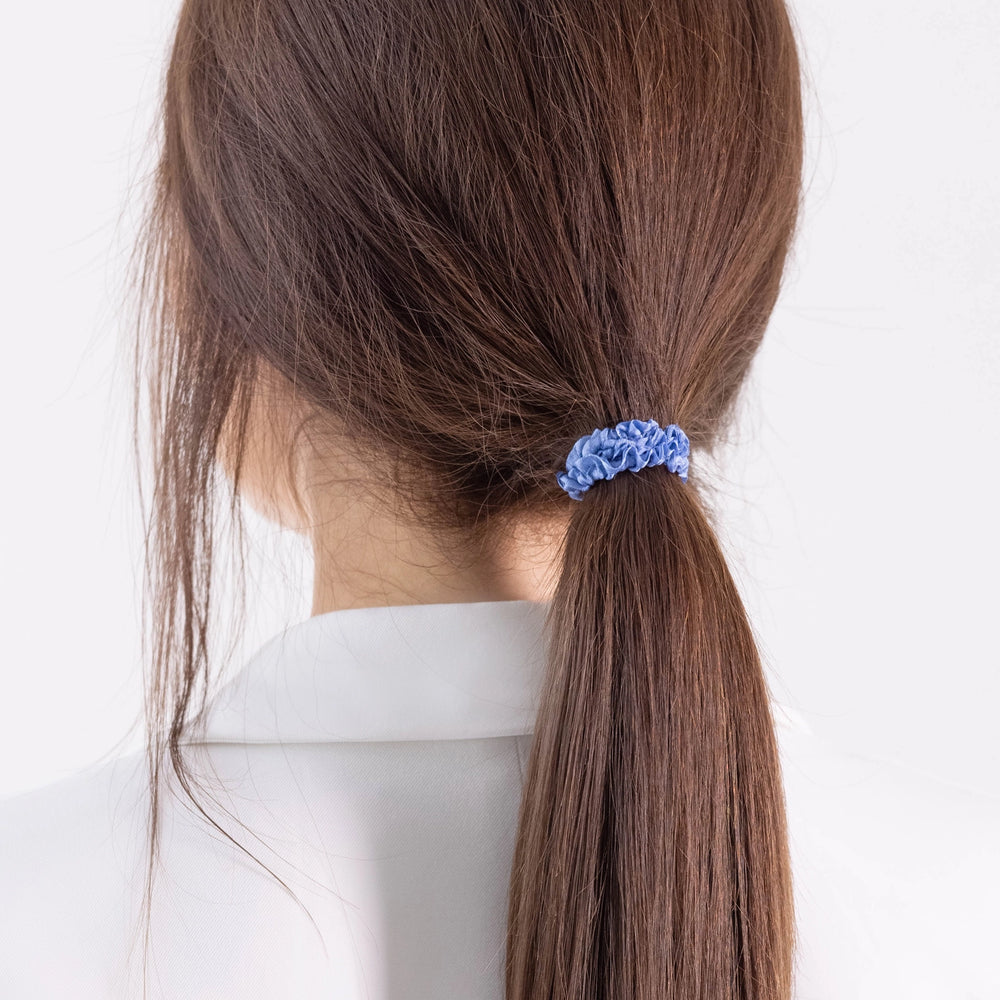 
                  
                    A dark-haired girl in white jacket, view from the back, details, with classic ponytail is wearing Malkiele designer light blue silk gentle hair tie, name Finesse.
                  
                