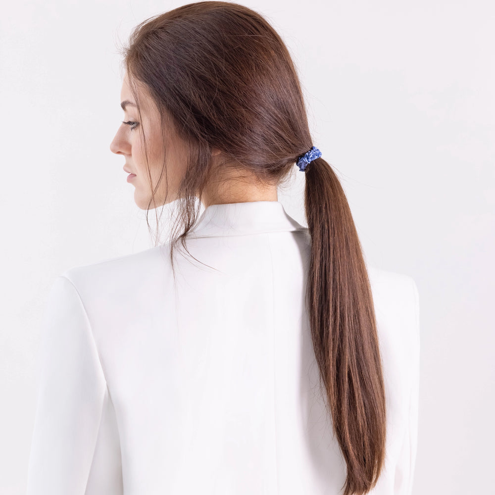 
                  
                    A dark-haired girl in white jacket, side view, with classic ponytail is wearing Malkiele designer light blue silk gentle hair tie, name Finesse.
                  
                