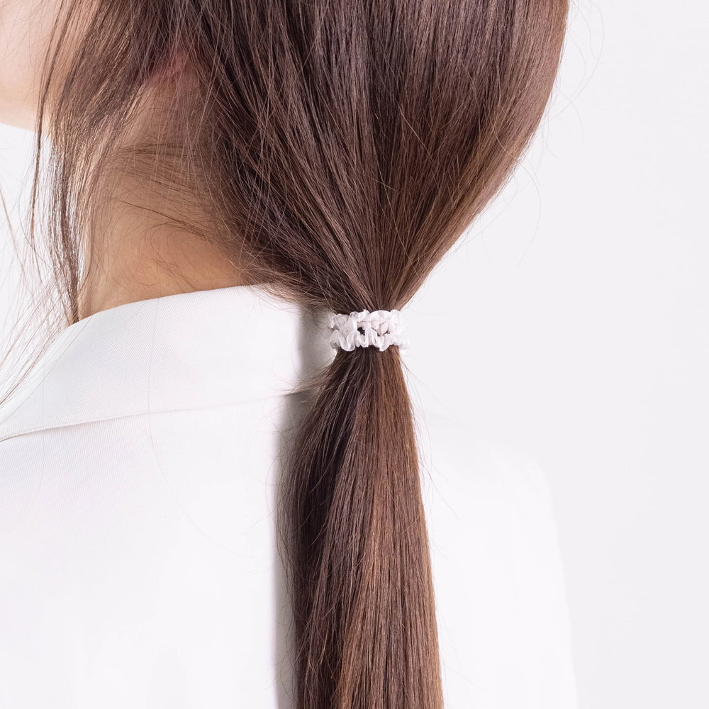 
                  
                    A dark-haired girl in white jacket, view from the back, details, with classic ponytail is wearing Malkiele designer bridal white silk gentle hair tie, name Finesse.
                  
                