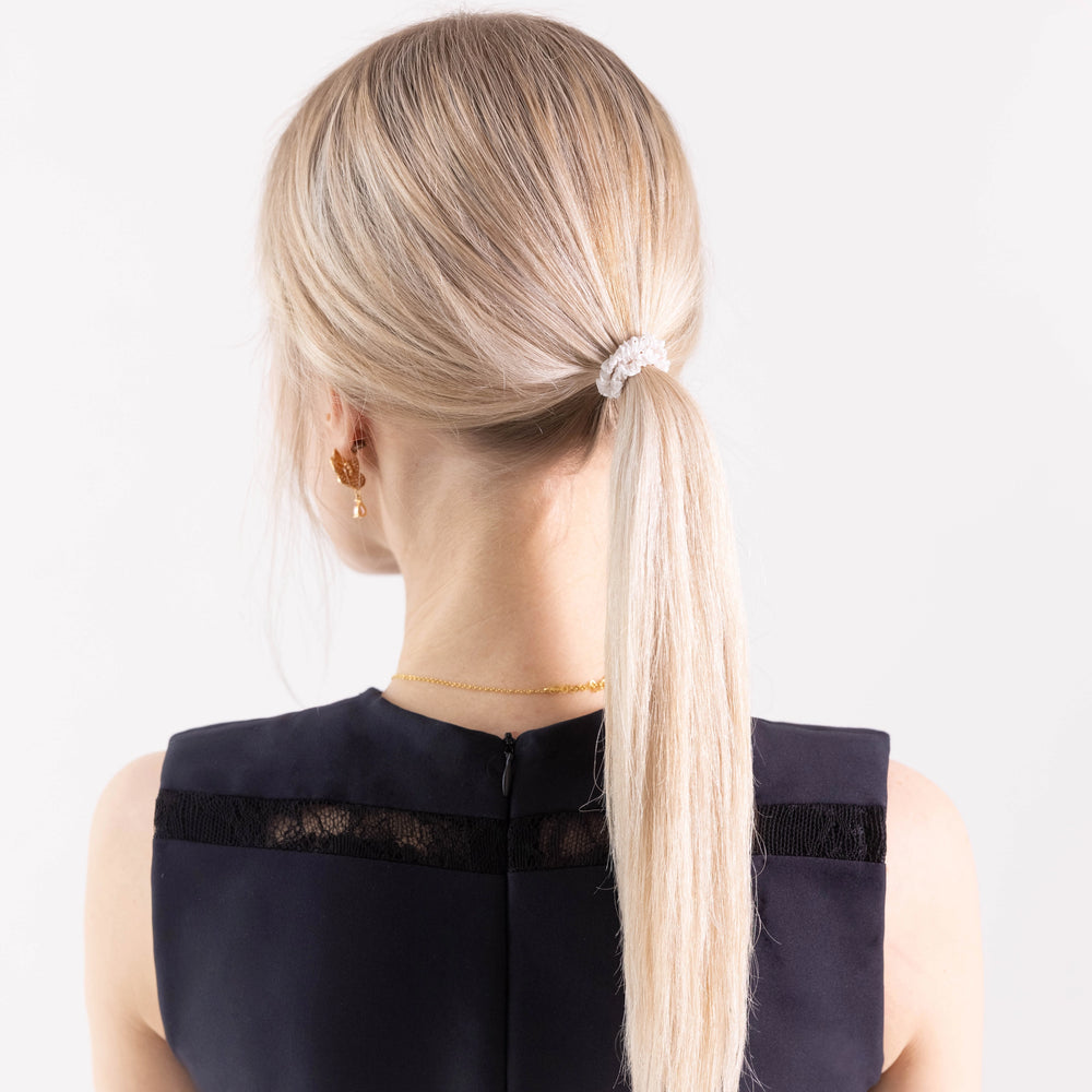 
                  
                    A blonde-haired girl in black dress, view from the back, with classic ponytail is wearing Malkiele designer white silk gentle hair tie, name Finesse.
                  
                