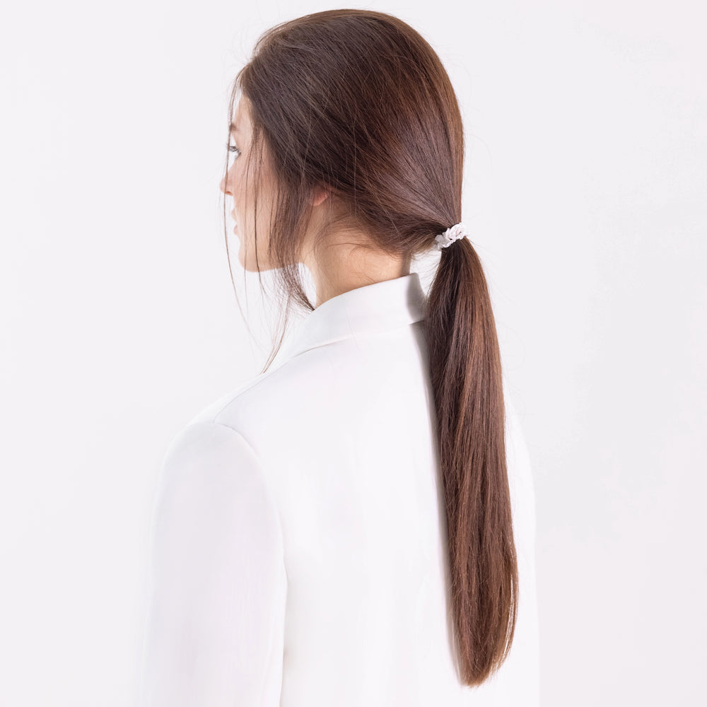 
                  
                    A dark-haired girl in white jacket, view from the back, with classic ponytail is wearing Malkiele designer bridal white silk gentle hair tie, name Finesse.
                  
                