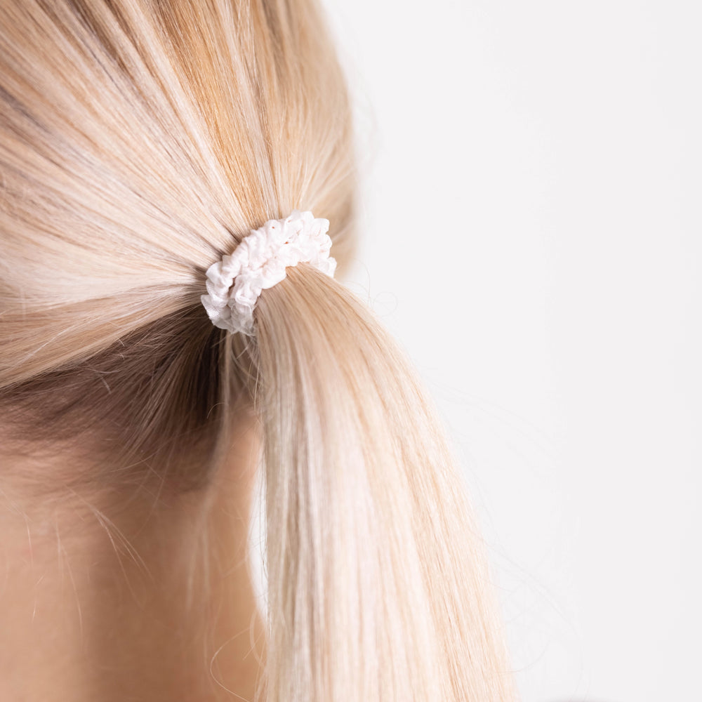 
                  
                    A blonde-haired girl, view from the back, details, with classic ponytail is wearing Malkiele designer white silk gentle hair tie, name Finesse.
                  
                