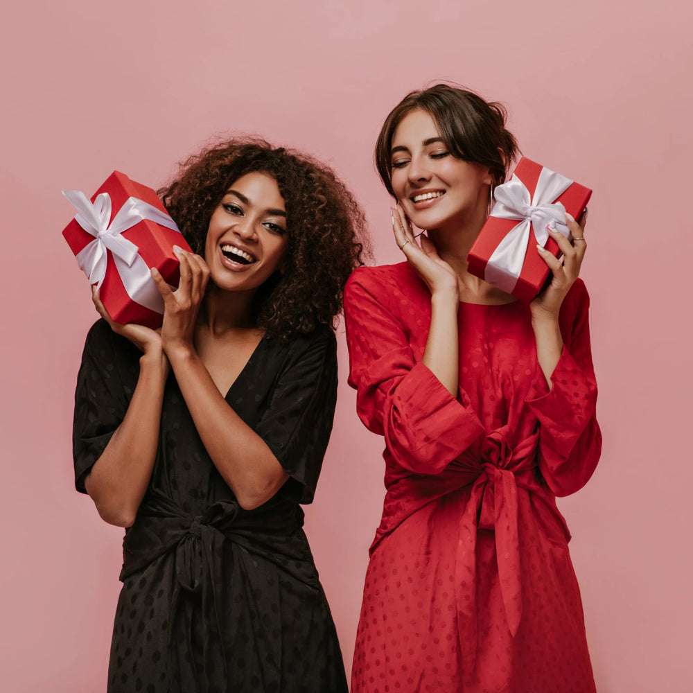 
                  
                    Two dark-haired happy girls are holding gifts, red boxes with white ribbon.
                  
                