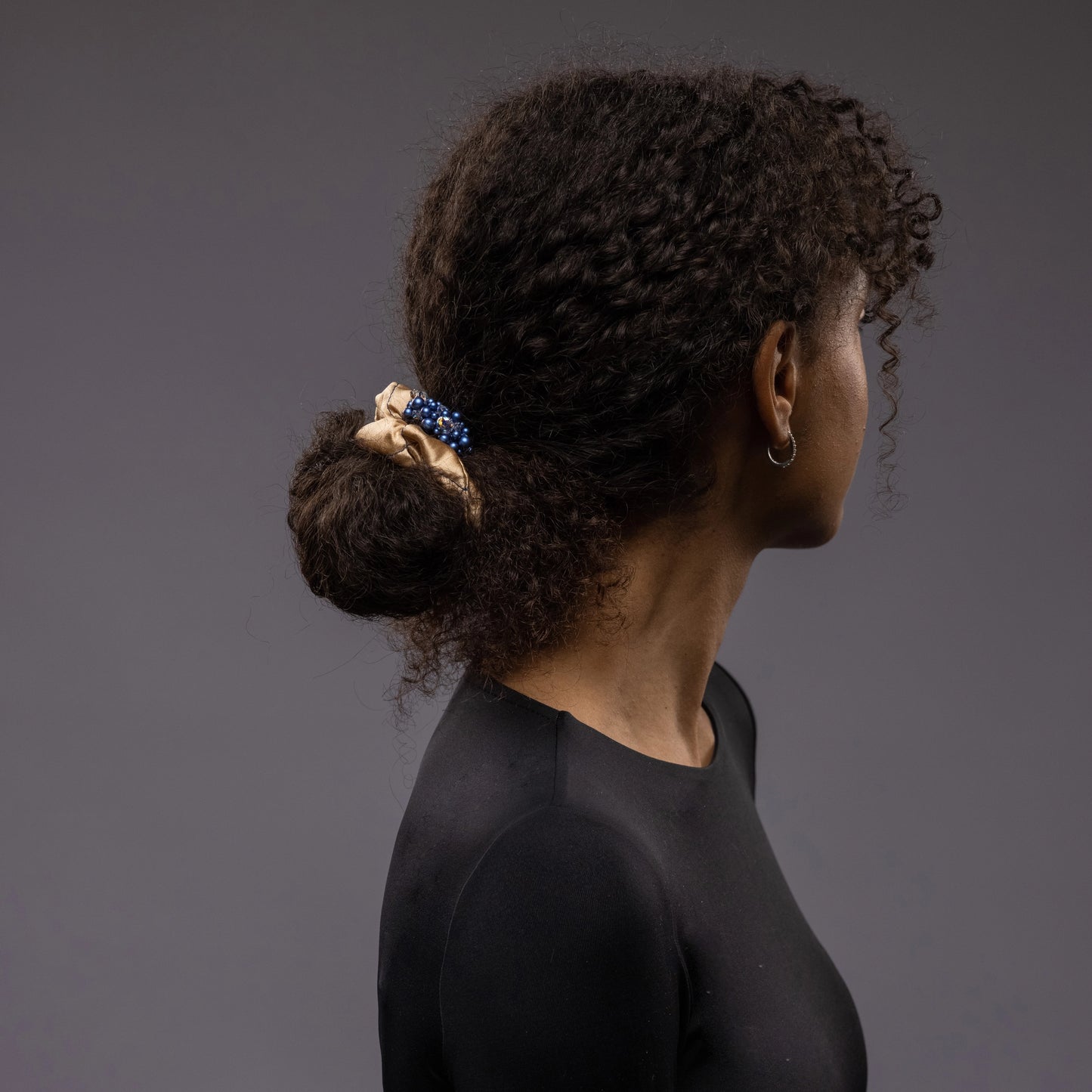 A dark-haired African woman is wearing Malkiele silk scrunchie with pearls in beige, name Glowing