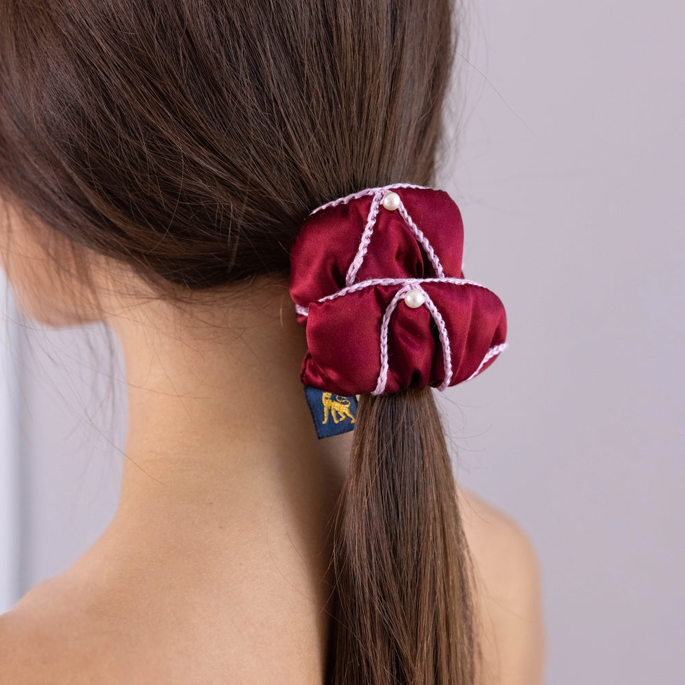 A dark-haired woman, view from the back, with stylish ponytail is wearing Malkiele designer burgundy silk scrunchie, embellished with 6 white pearls from Swarovski and pink silk knit ribbon, name Majestic.