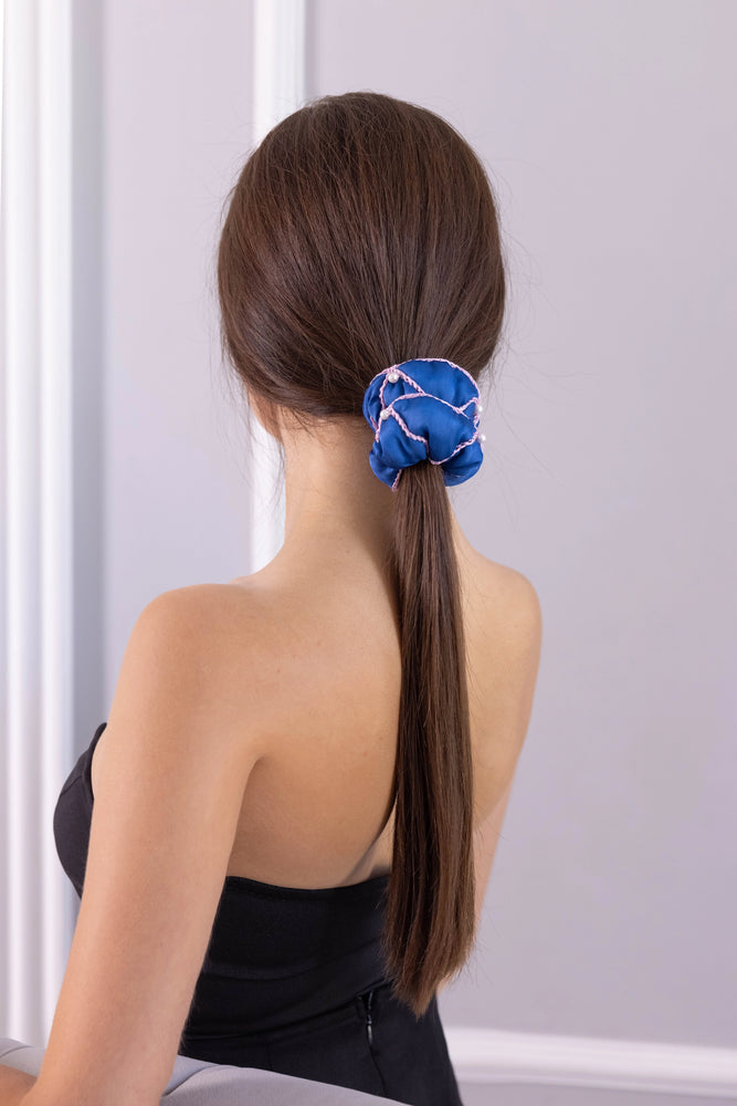 
                  
                    A dark-haired woman, view from the back, with stylish ponytail is wearing Malkiele designer royal blue silk scrunchie, embellished with 6 white pearls from Swarovski and pink silk knit ribbon, name Majestic.
                  
                