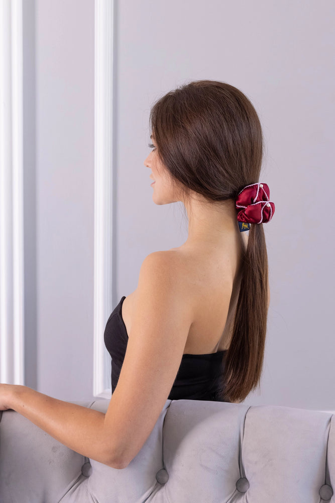 
                  
                    A dark-haired woman, view from the back, with stylish ponytail is wearing Malkiele designer burgundy silk scrunchie, embellished with 6 white pearls from Swarovski and pink silk knit ribbon, name Majestic.
                  
                