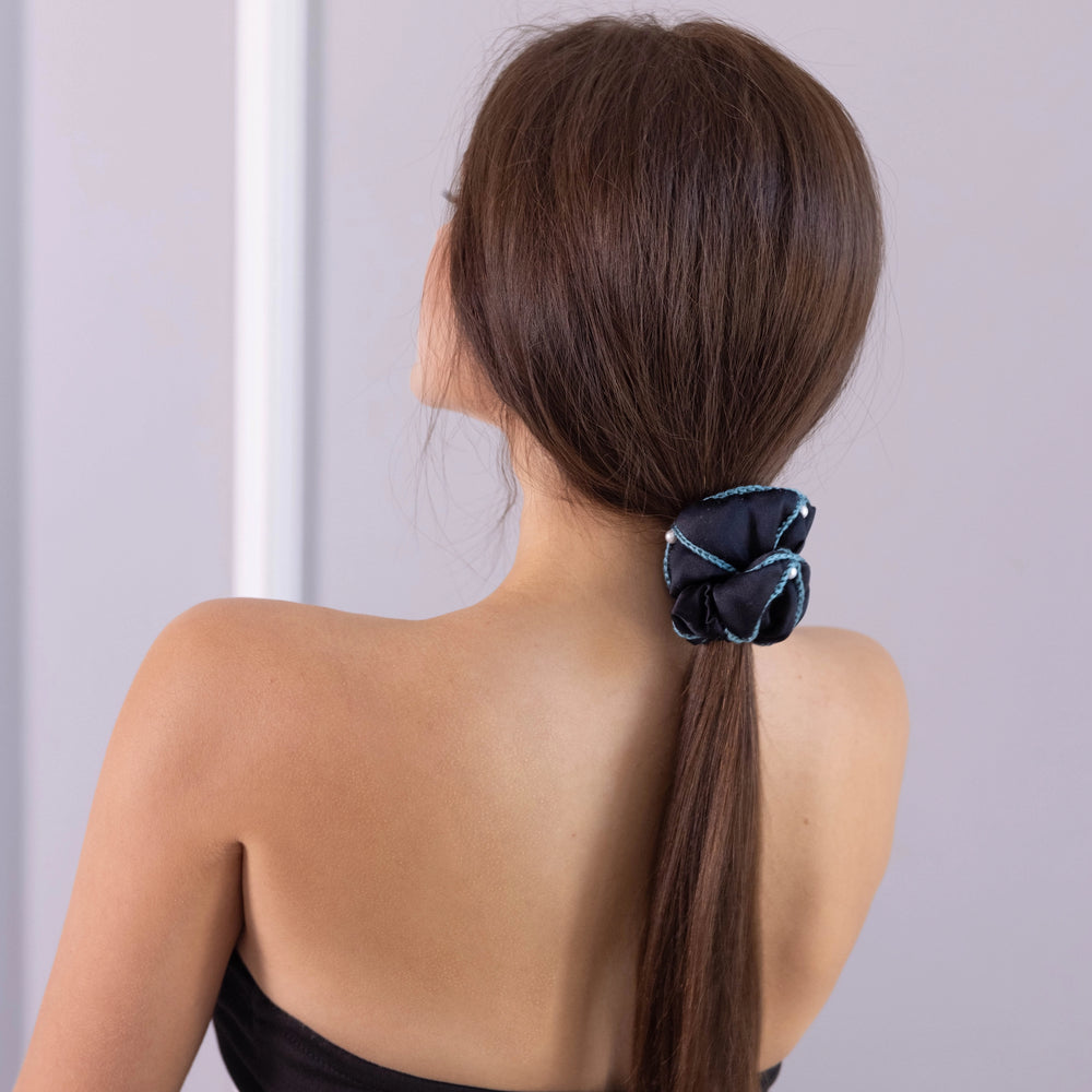 
                  
                    A dark-haired woman, view from the back, with stylish ponytail is wearing Malkiele designer black silk scrunchie, embellished with 6 white pearls from Swarovski® and green silk knit ribbon, name Majestic.
                  
                