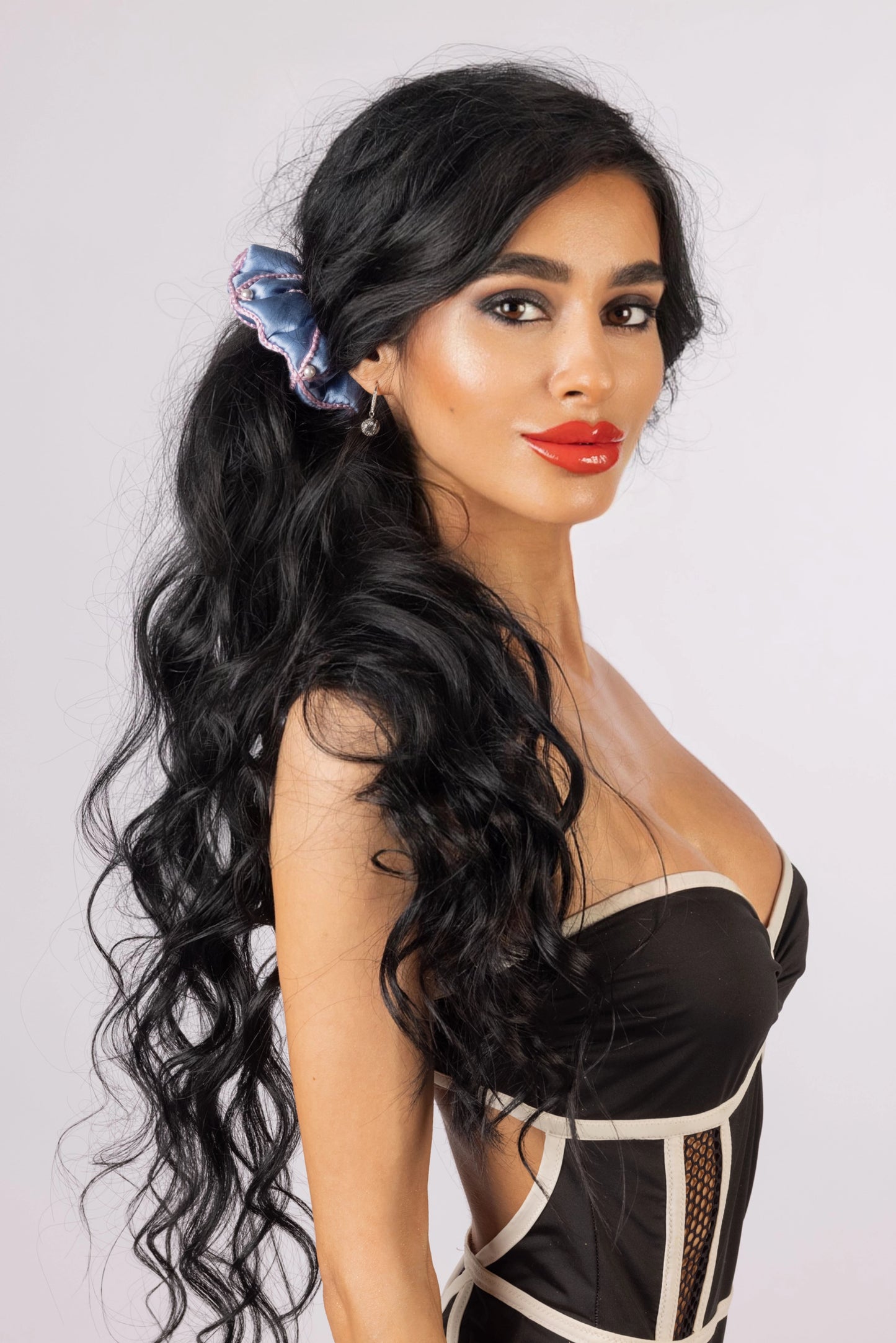 
                  
                    A black-haired woman, with stylish ponytail is wearing Malkiele designer light blue silk scrunchie, embellished with 6 white pearls from Swarovski and pink silk knit ribbon, name Majestic.
                  
                