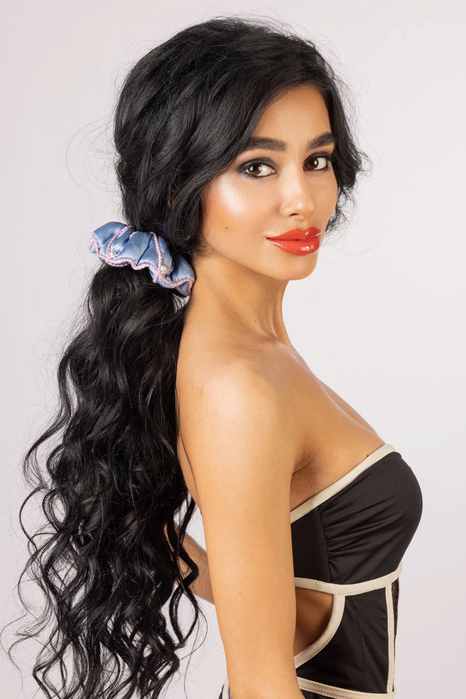 
                  
                    A black-haired woman, with stylish ponytail is wearing Malkiele designer light blue silk scrunchie, embellished with 6 white pearls from Swarovski and pink silk knit ribbon, name Majestic.
                  
                