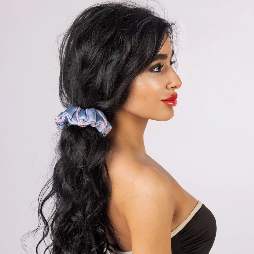 A black-haired woman, with stylish ponytail is wearing Malkiele designer light blue silk scrunchie, embellished with 6 white pearls from Swarovski and pink silk knit ribbon, name Majestic.