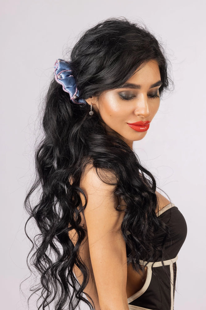 
                  
                    A black-haired woman, with stylish ponytail is wearing Malkiele designer light blue silk scrunchie, embellished with 6 white pearls from Swarovski and pink silk knit ribbon, name Majestic.
                  
                