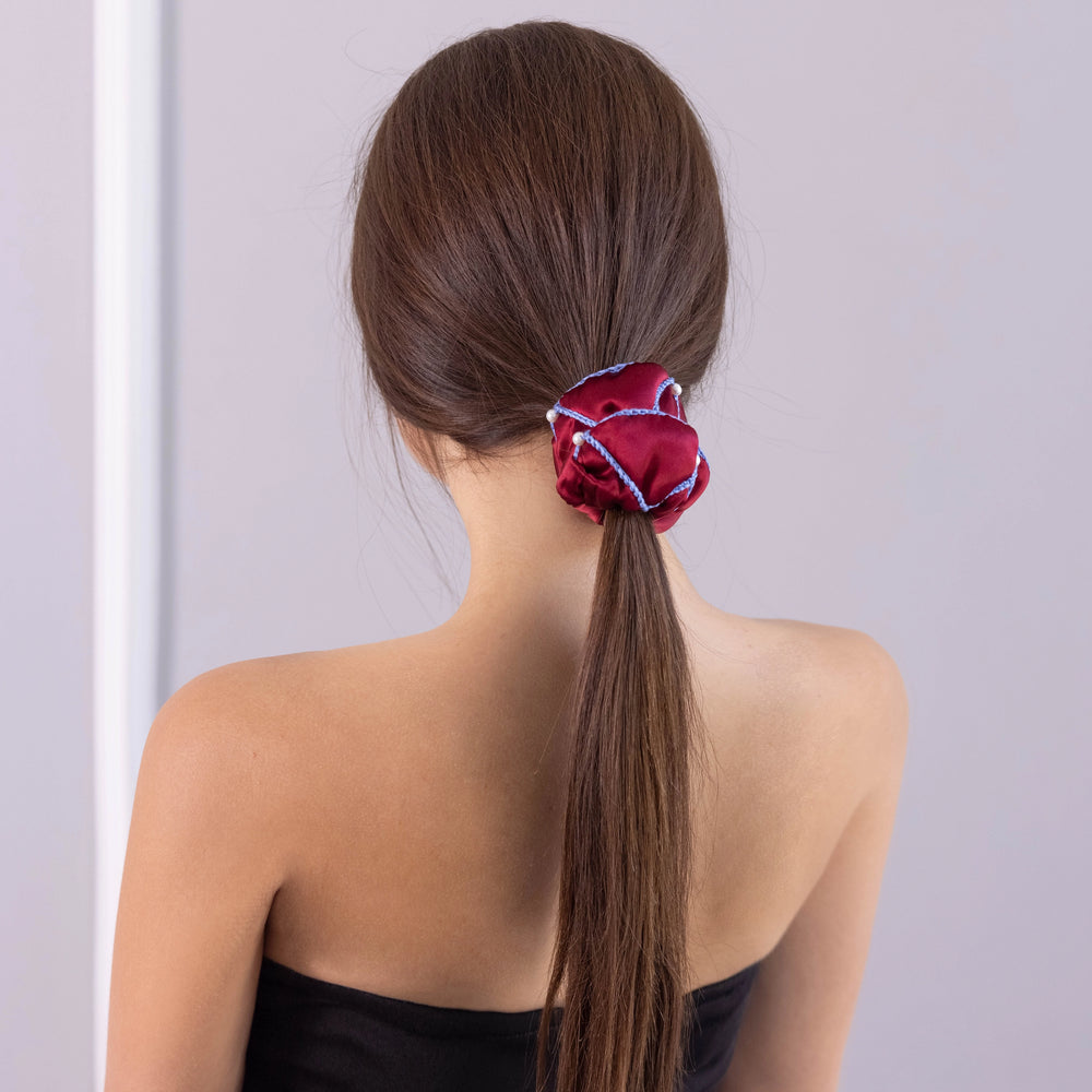 A dark-haired woman, view from the back, with stylish ponytail is wearing Malkiele designer burgundy silk scrunchie, embellished with 6 white pearls from Swarovski and light blue silk knit ribbon, name Majestic.